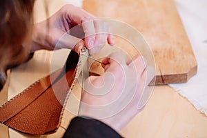 Detail shot of woman`s hands sewing a brown piece of leather with a needle