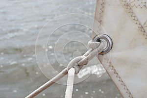 Detail of a silver ring eyelet in a white sail, attached to a white rope