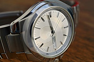 Detail of silver watch with white clock dial on the wooden background as a symbol of time or exactness