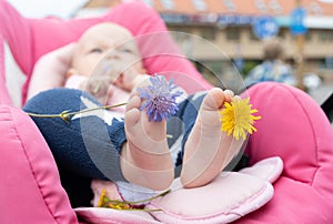 Detail of small infant feet lying in a stroller. bare feet of a baby and flowers between his toes