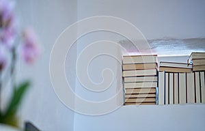 Detail of stack of books in a space in a textured white wall of a room in a modern house, unsharp flower in the foreground