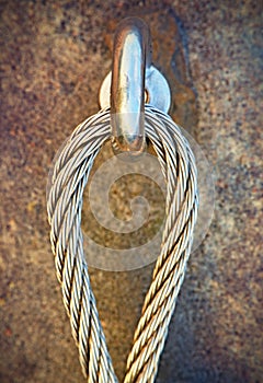 Detail of steel bolt anchor eye in rock. The end knot of steel rope. Climbers path in rocks via ferrata. Iron twisted rope fixed