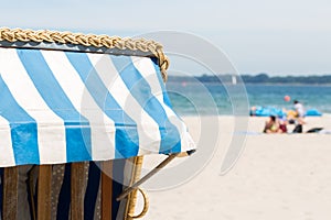 Detail of a Strandkorb wicker beach chair, Tourists in the background.