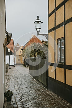 Detail of the street lamp with ornaments hanging on the yellow wall of the old house in the empty street with granite road,