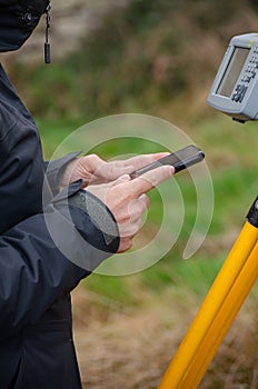 detail of a surveyor's hands configuring the total station with the mobile phone, topography works