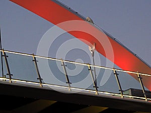 Detail of a suspended pedestrian overpass at dusk, lit from below in red