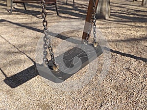 Detail of swing bench with metal ropes on sand ground of playground. Closeup of plastic gray swing for kids on the park