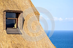 Detail of a thatched roof house using reed grass as building material. Windows visible and the ocean in the background.