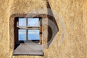 Detail of a thatched roof house using reed grass as building material. Windows visible and the ocean in the background.