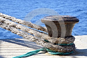 Detail of thick boat ropes tied to an old rusty bollard