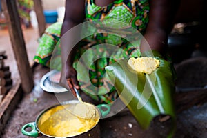 Detail of traditional african corn foufou on plantain leaf held by black woman cooking in humble home kitchen