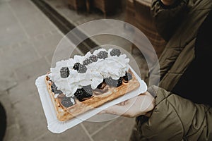 Detail of the Traditional Polish specialty gofry with whipped cream and blackberries on woman hand