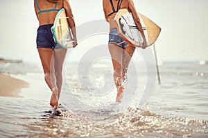 Detail of two female surfers running on the  beach holding surfboards