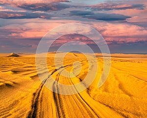 Detail of tyre tracks in sand desert with colorful sky