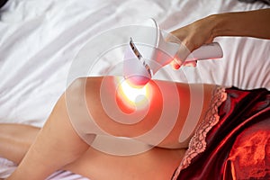 Detail of an unidentifiable women using a silk nightgown using an intense pulsed light machine to remove hair from her legs