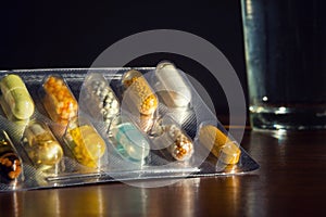 Colorful pills medicine capsule with glass of water on table