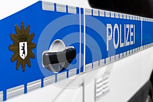 Detail view of a Berlin police car with the word `Polizei` and the blurred Berlin city coat of arms in the foreground