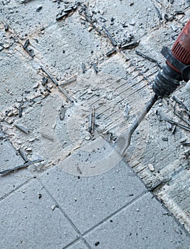 Construction worker using a handheld demolition hammer and wall breaker to chip away and remove old floor tiles during renovation photo