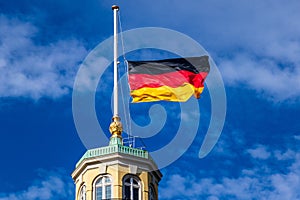 Detail view on German Flag at Halfmast, auf Halbmast, on the tower roof of Castle Karlsruhe, blue sky in background. Germany