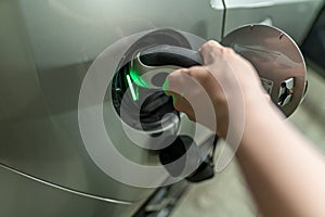 Detail view at a mans hand with is plugin the electric charging wire and plug into his e-automobiles fuel cap. Green