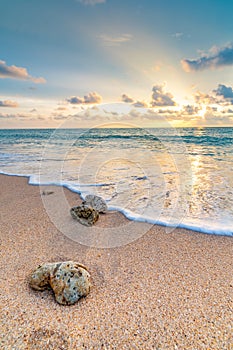 Detail view of rock on the beach, placed in the sand, with big water wave from the sea. Beautiful sunset above ocean with soft