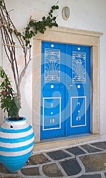 Detail view of a traditional Greek white facade with blue door and flower pot in Naxos island