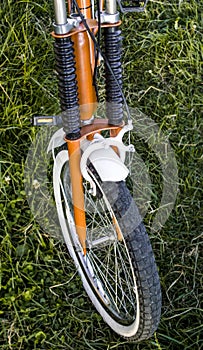 Detail of a vintage orange and white bicycle`s wheel oin the grass