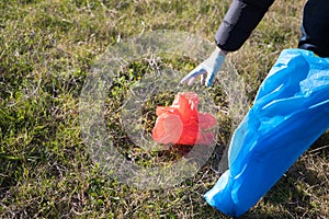 Detail of a volunteer\'s hand picking up a red plastic bag from the forest. Concept of Earth Day and World Environment
