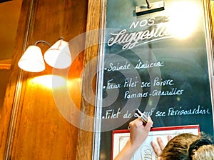 Detail of a waitress writing the menu of the day in a board inside a bistrot, Paris, France