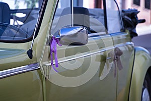 Detail of wedding ornament placed on the silver rearview mirror of a metallic green convertible car
