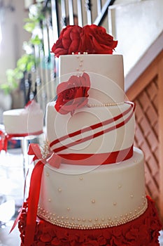 Detail of white layered wedding cake with red edible flowers