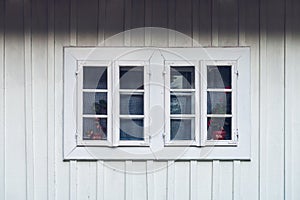 A detail of a white window against a white facade made of wooden planks. Country window