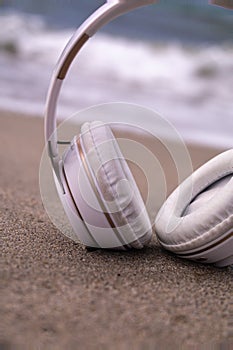 detail of white wireless bluetooth headphones on the sand on the shore of the beach with selective focus rest concept