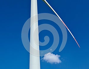 Detail of wind power plant with post and a single blade in blue sky with a single cloud