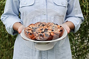 A woman hands holding home baked apple pie with blueberries