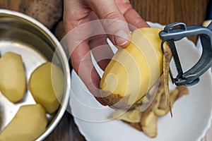 Detail of woman hands peeling fresh yellow potato with kitchen p