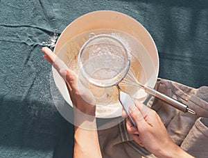 Detail of a woman hands sifting flour with a strainer on a bowl. Cooking and ingredients concept