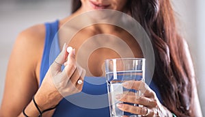 Detail of a woman holding a white pill and a glass of water