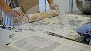 Detail of woman`s hand rolling out a dough with a rolling pin while making homemade pasta. Woman`s hands rolling dough