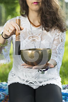 Detail of a woman`s hands holding and playing a Tibetan singing bowl