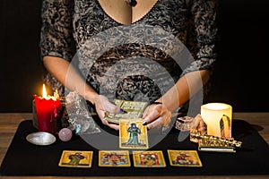 Detail of a woman`s hands placing tarot cards on a black card table