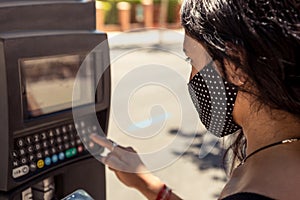 Detail of a woman wearing a protective facial mask using a parking machine in the street. Coronavirus protection in the new normal