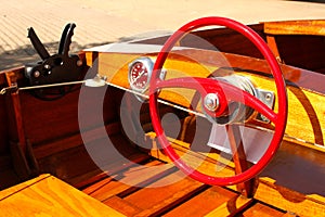 Detail of Wood Speed Boat with Bright Red Steering Wheel at Dock with gears and speedometer