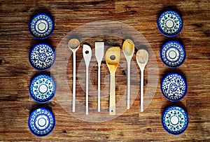 Detail of wooden cooking spoons and painted ornate plates on textured wooden table, vintage style