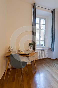 Detail of a wooden desk and an elegant blue chair and a bright window on the right. Ideal location for smartworking photo