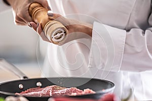Detail of a wooden pepper grinder putting spice on cut of pork in a pan