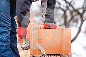 Detail of worker, bricklayer construction engineer fixing bricks and building walls at new house on a winter day