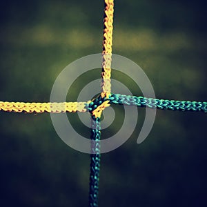 Detail of yellow blue crossed soccer nets, soccer football in goal net with green grass on playground in the background.