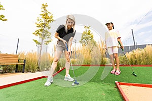 Detail of young woman and daughter playing mini adventure golf on a beautiful sunny summer day
