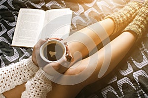 Detail of young woman and sun light. Woman keep a coffee cup and read a book.